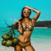 beautiful tanned girl in trendy bathing suit sunglasses stands with a bunch of coconuts